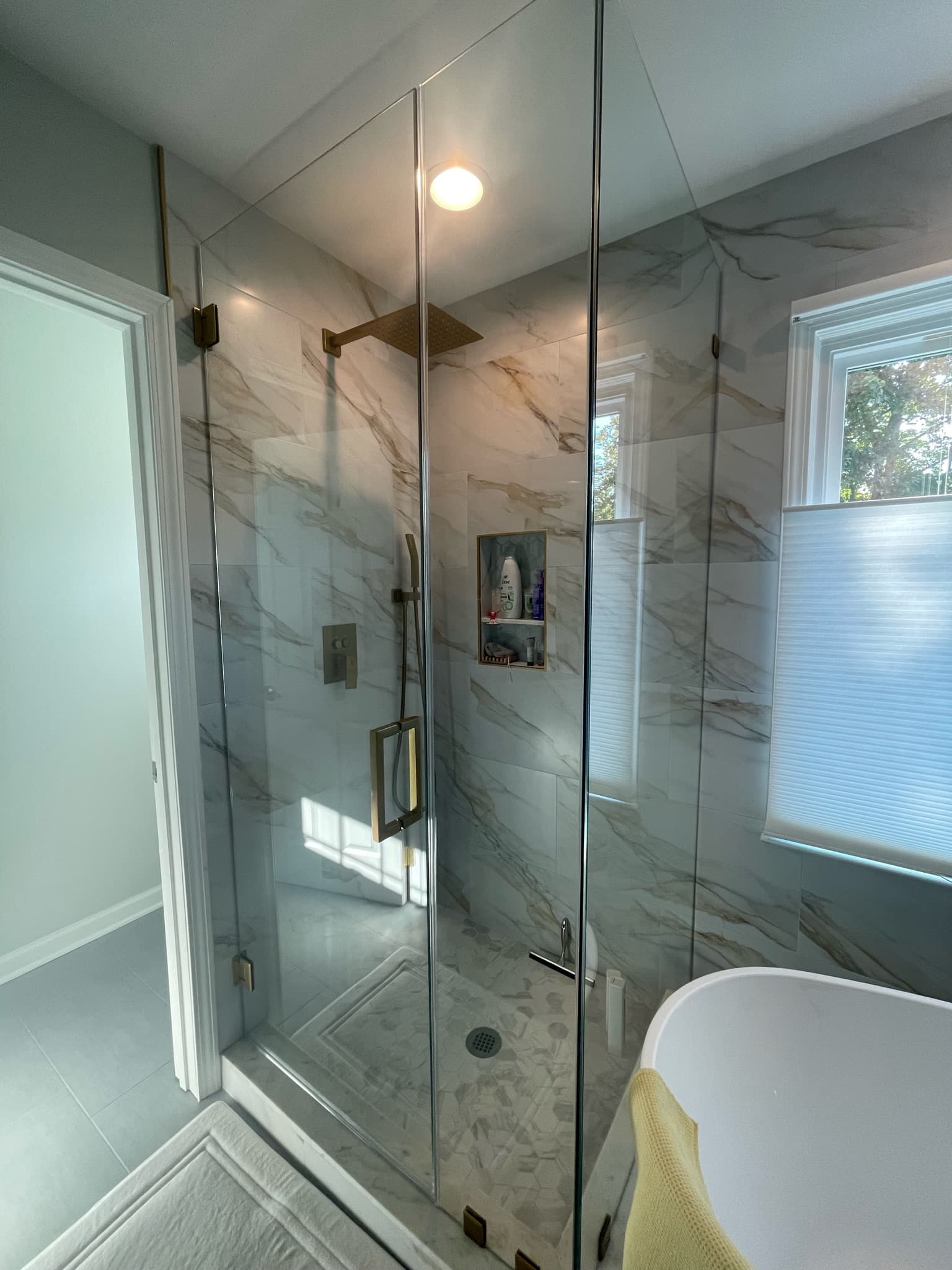 Glass-enclosed marble tile shower with built-in niche and custom penny mosaic floor in Charlotte NC